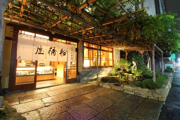 藤棚の下に明かりのともる和風の店構え。白いのれんに「船橋屋」と染め抜かれている