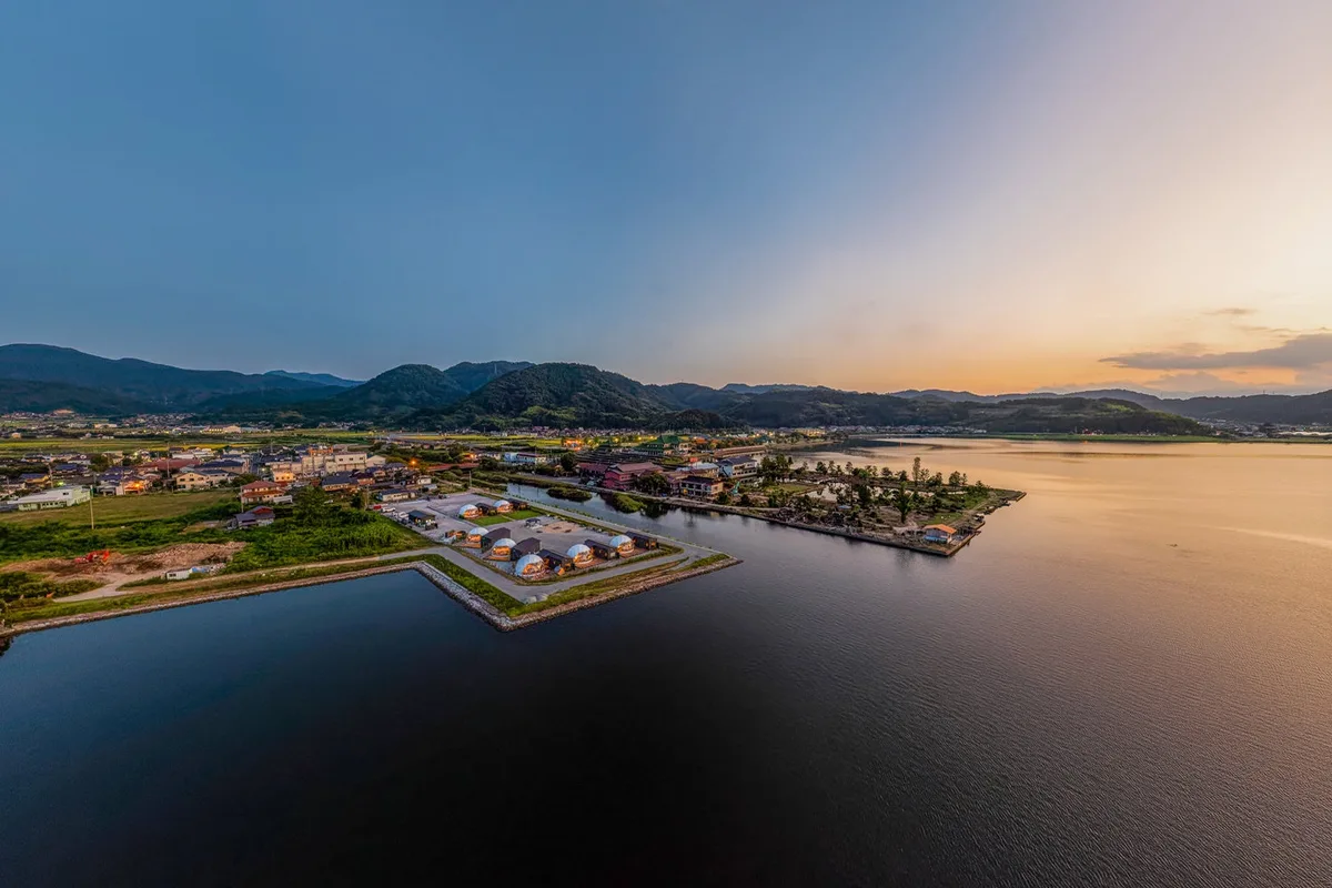 夕暮れの東郷湖畔に並ぶドーム型の客室を上空から捉えた全景。湖面がオレンジ色に染まっている