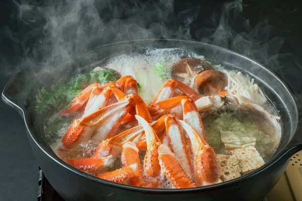 湯気の立つカニ鍋。ズワイガニの脚、きのこ、豆腐、春菊が土鍋に入っている