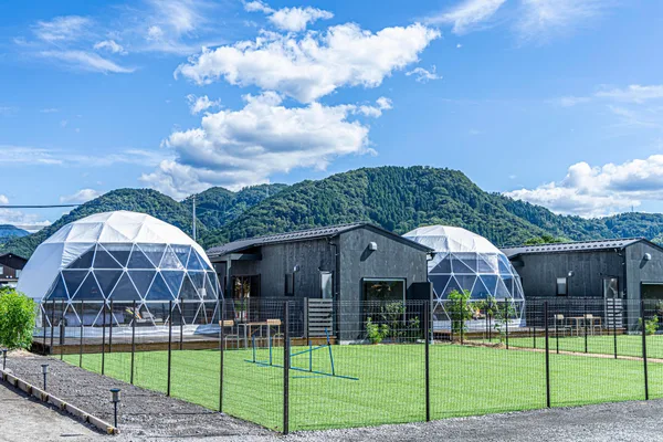 ドーム型客室と黒い外観の棟、手前に芝生の運動スペースと犬用の障害物