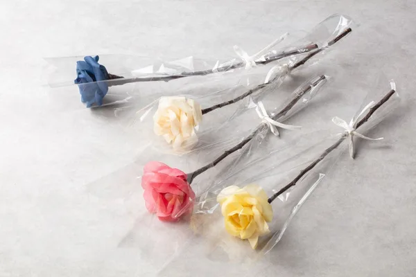 透明な袋に入った4本の花。かんなくずで作られた花びらが青、白、桃、黄に染められている
