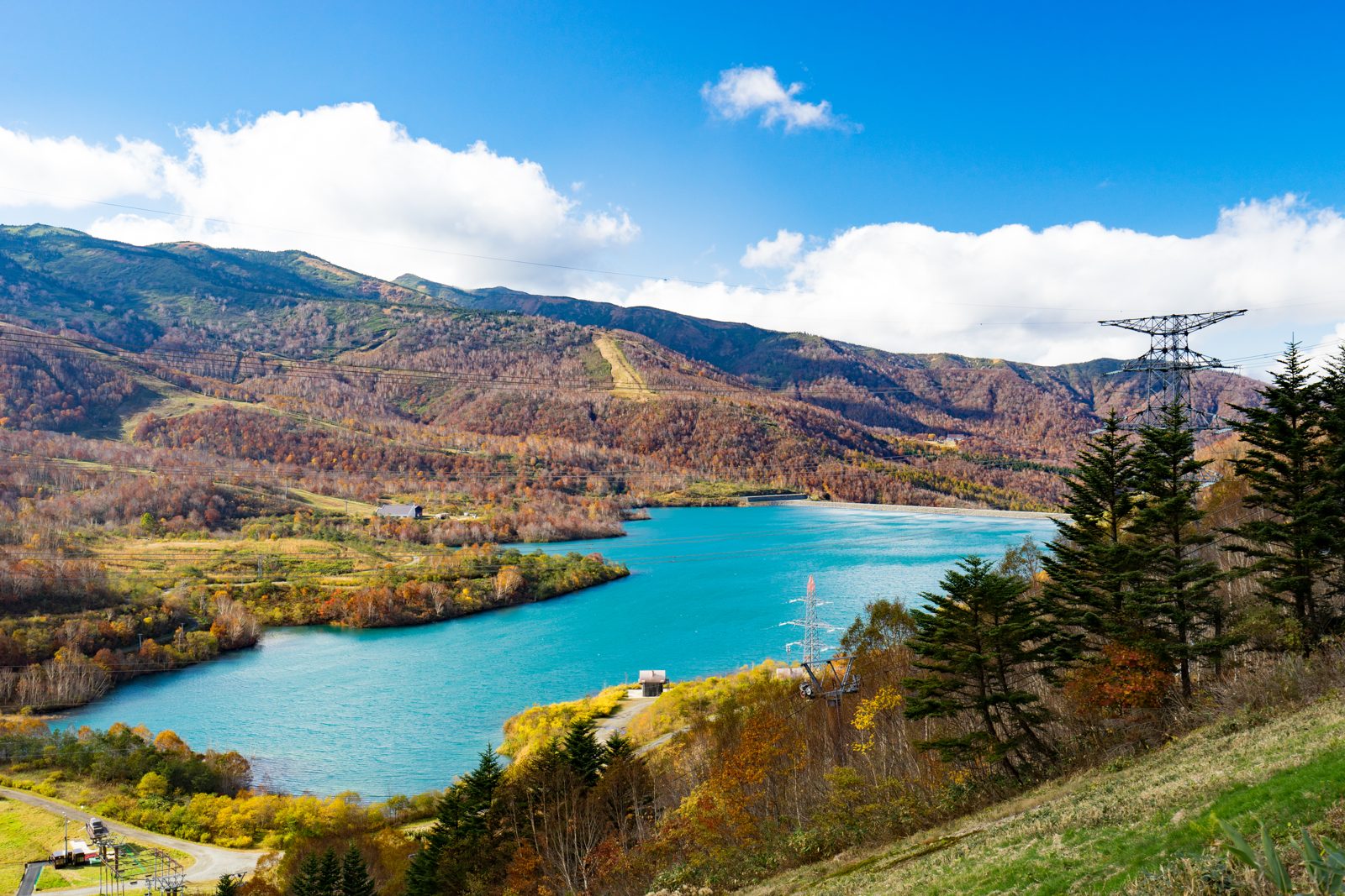 田代湖と周りの山の紅葉。青い湖面の奥で山肌が橙や黄色に色づく