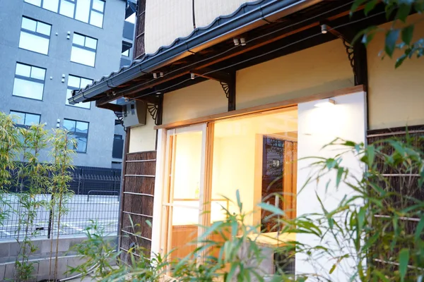 瓦屋根と土壁の町家。ガラス戸の奥に明かりがともり、手前に竹が植わる