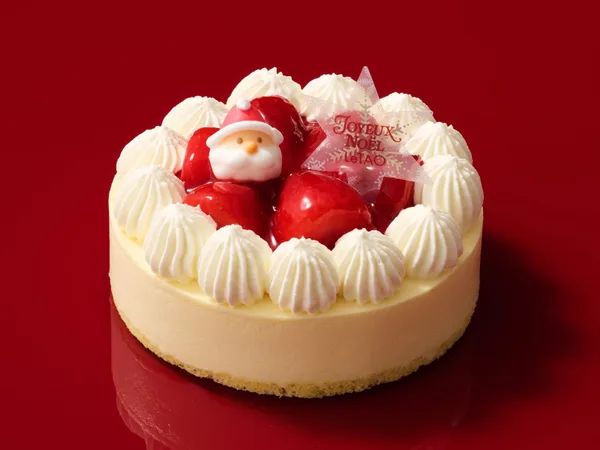 白い生クリームの絞りに囲まれ、中央に苺とサンタの飾りをのせた丸いケーキ