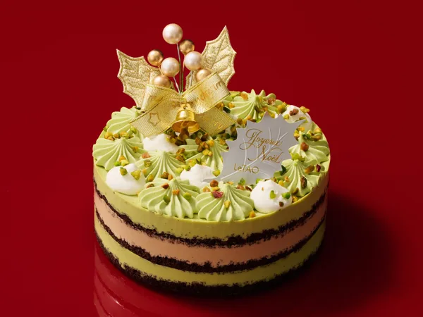 黄緑色のクリームの絞りと刻みピスタチオをのせ、側面に緑と茶の層が見えるケーキ