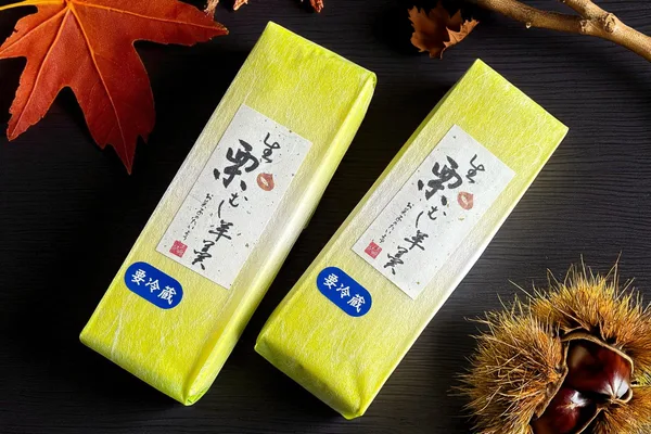 「生栗むし羊羹」と書かれた黄緑色の包装の商品2本と、紅葉の葉、栗のいが