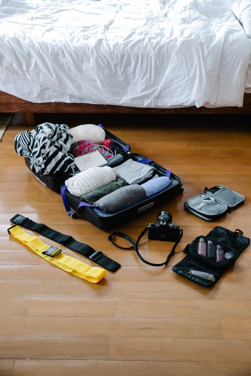 開いたスーツケースと旅行の荷物を床に並べたイメージ写真