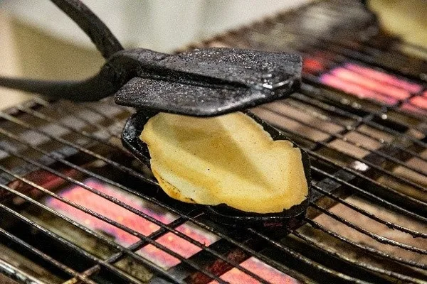 網の上の火で、焼型に挟んだいかせんべいを焼いているところの接写