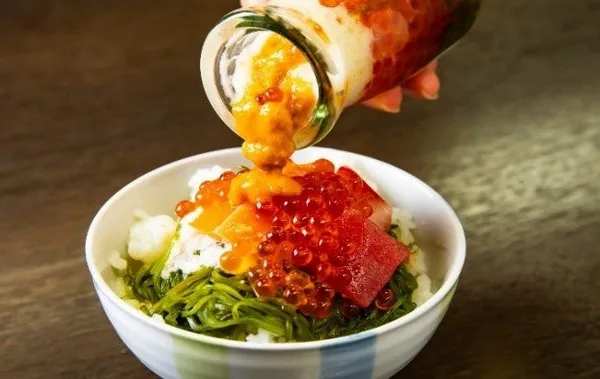 牛乳瓶から丼のご飯へ、いくらやまぐろ、うに、めかぶなどの海鮮を盛り付けているところ