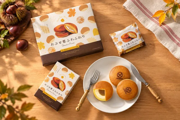 木のテーブルに置かれた白い箱と個包装、白い皿にのった丸い菓子3個と断面。周りに栗と紅葉した葉