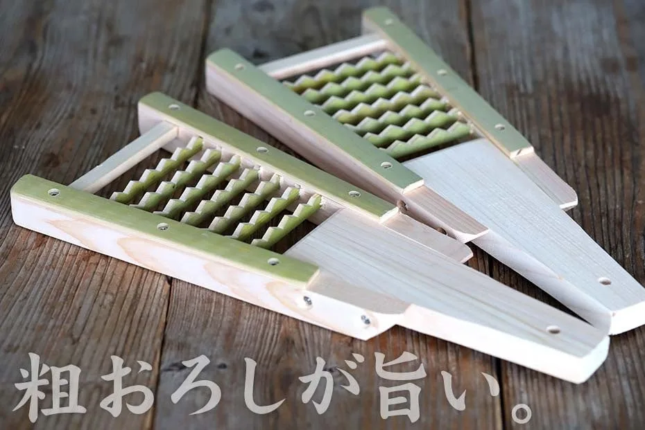 木の台に並んだ3つの鬼おろし。緑がかった竹の鬼歯がV字に並び、ヒノキの本体と持ち手が見える。画面下に「粗おろしが旨い。」の文字がある
