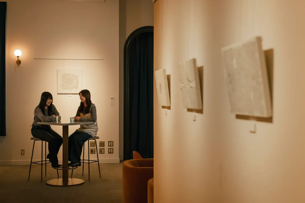 アールデコ調のホテル館内で壁面作品を眺めながらテーブル席で過ごす来館者