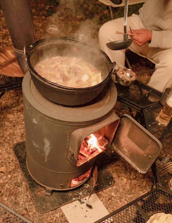 薪ストーブの上で温まる鍋と、薪の火